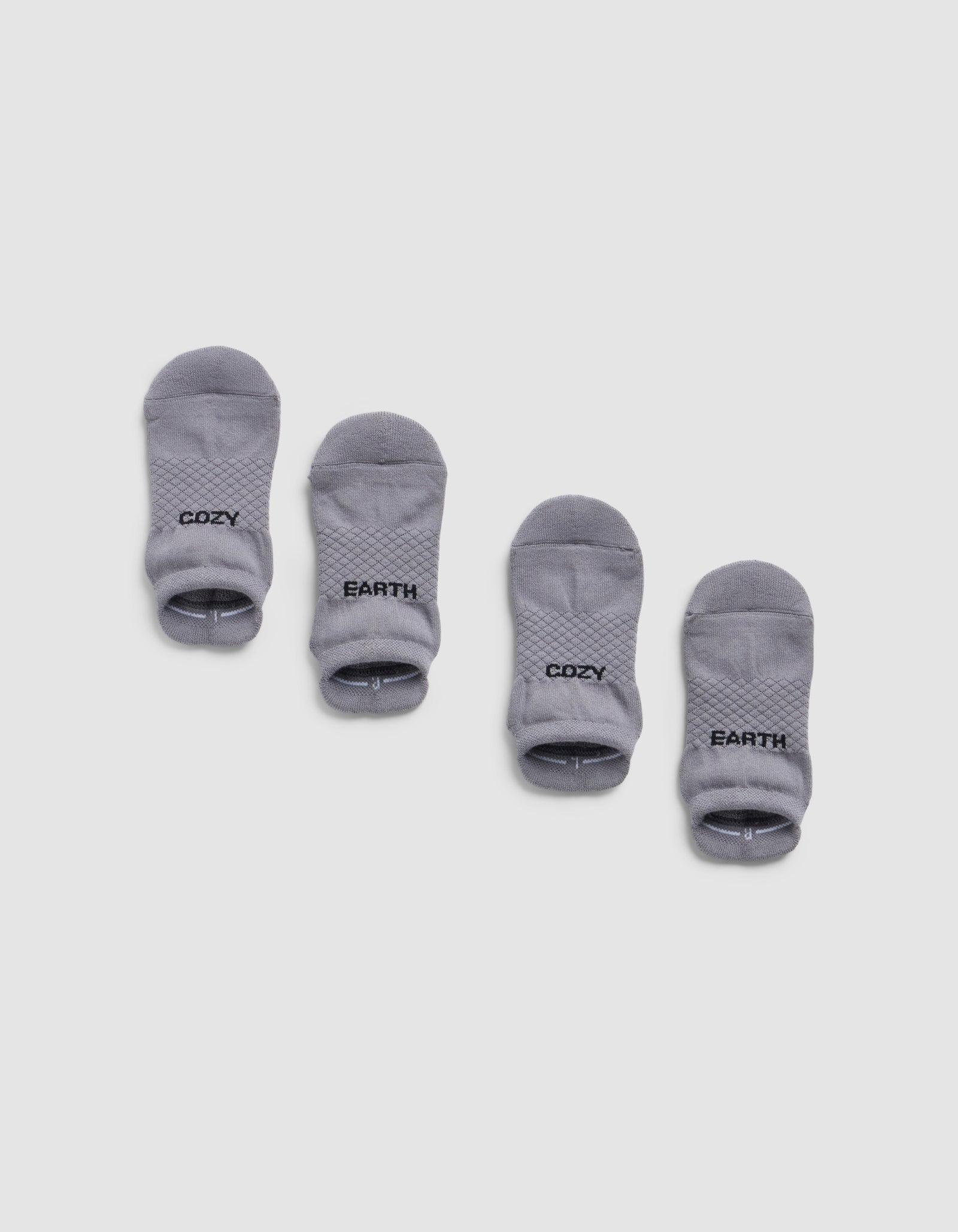 Four small gray Essential Ankle Socks by Cozy Earth are arranged in two pairs on a white background. The left pair has "COZY" and the right pair has "EARTH" printed in black text near the cuff.
