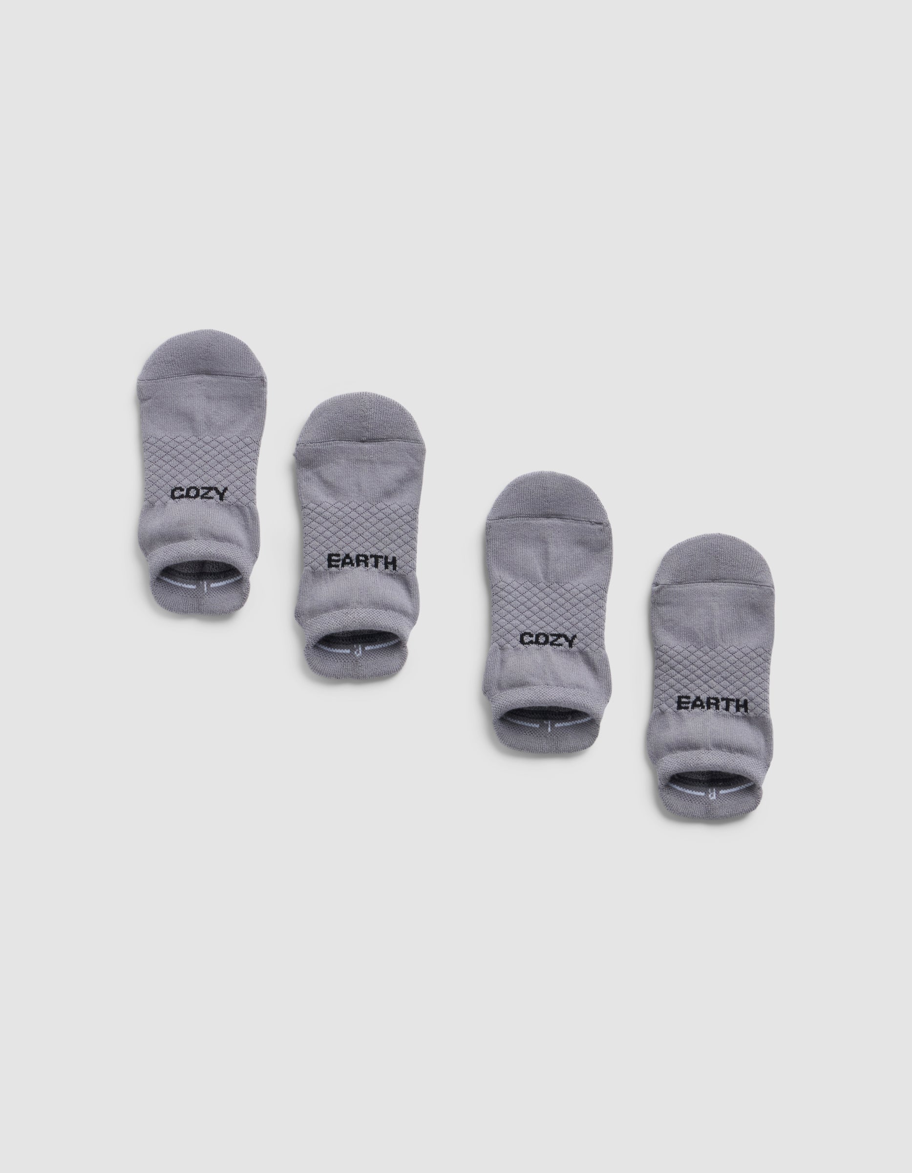 Four small gray Essential Ankle Socks by Cozy Earth are arranged in two pairs on a white background. The left pair has "COZY" and the right pair has "EARTH" printed in black text near the cuff.