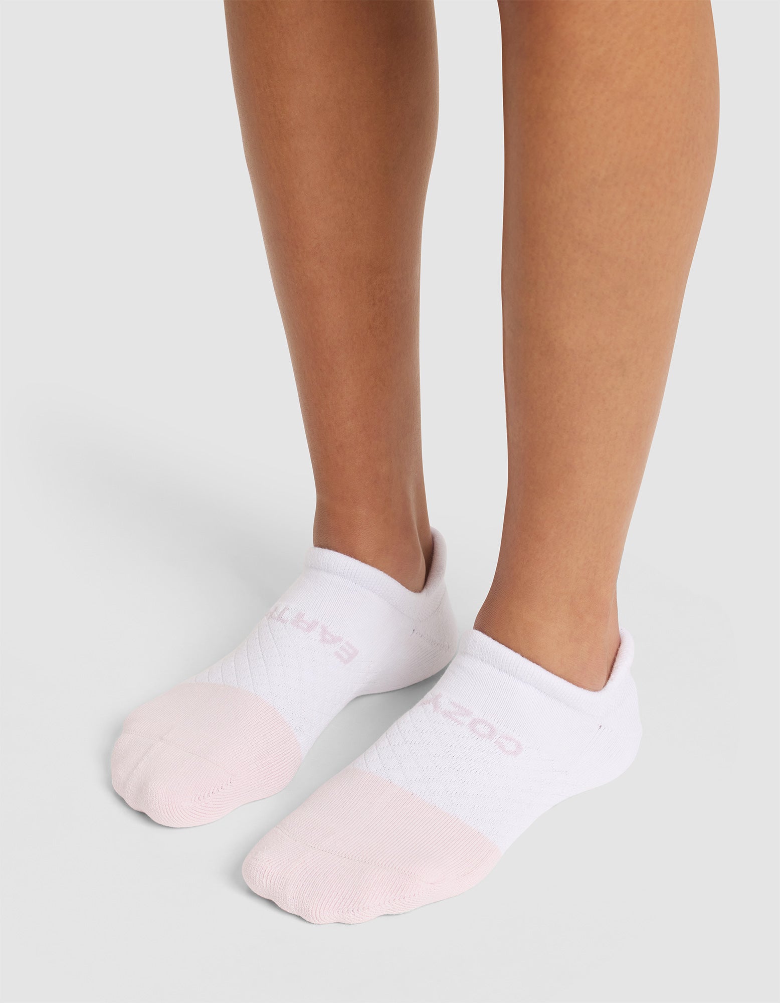 A person wearing Cozy Earth Essential Ankle Socks with pale pink toes stands on a light gray background, showing only their lower legs and feet. 