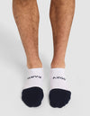 A person stands on a white background wearing Cozy Earth Essential Ankle Socks—white no-show socks with black toes; "BATH" is written on the left sock and "COZY" on the right in black letters. |Color:Spruce