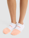 A person wearing Cozy Earth's Essential Ankle Sock—featuring white tops, peach toes, and red text near the cuff—stands on a light gray surface. |Color:Cantaloupe