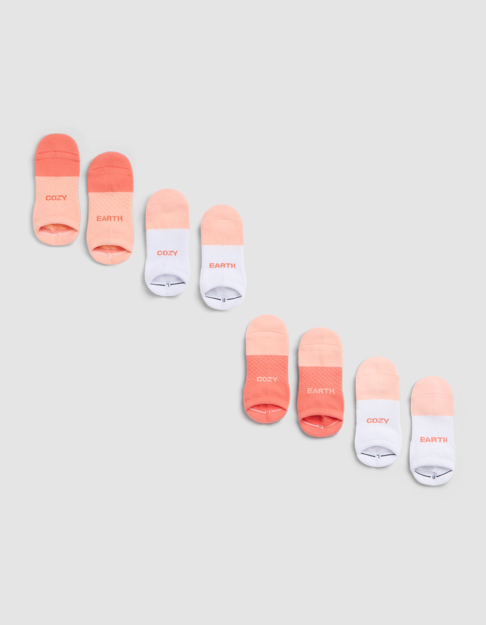 The Cozy Earth Essential Ankle Sock 4-Pack features socks in coral, peach, and white, each with "COZY" or "EARTH" near the toes, shown diagonally on a light gray background. 