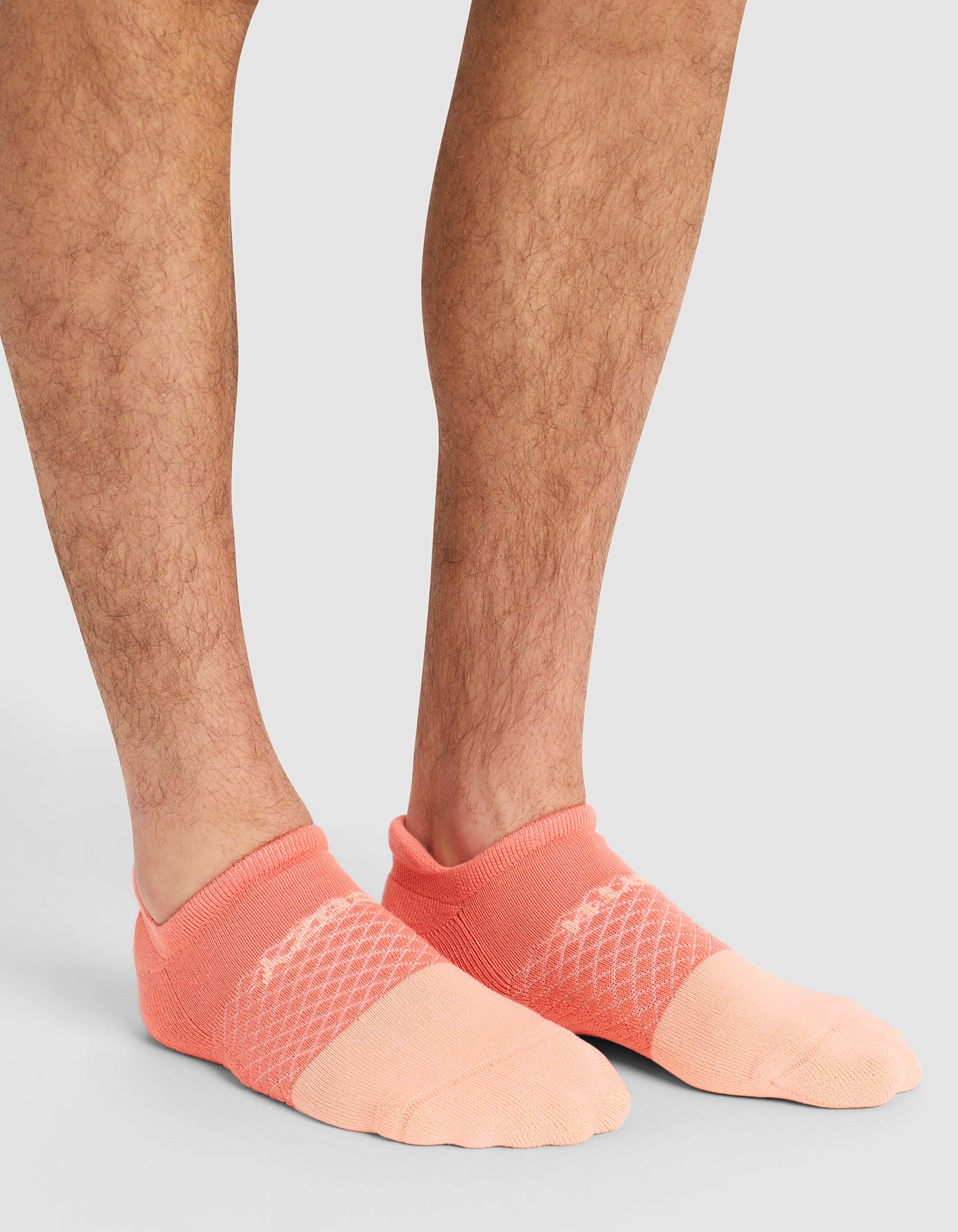 A close-up of a person's lower legs and feet wearing Cozy Earth Essential Ankle Socks in pink, standing on a light gray surface. 