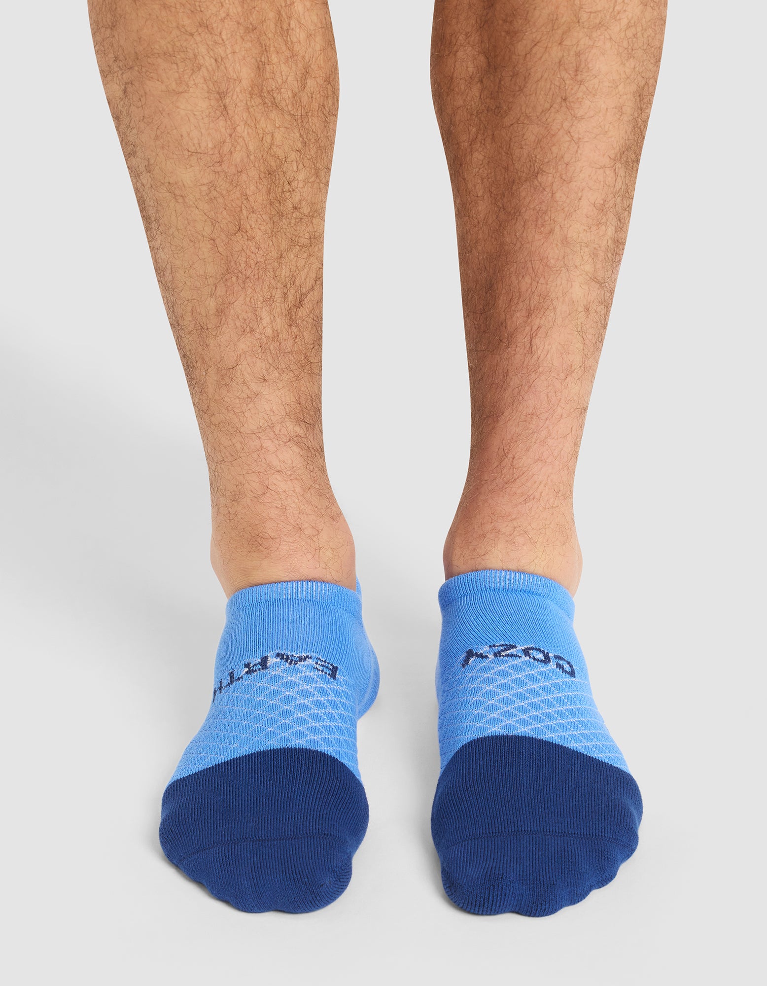 A pair of legs wearing Cozy Earth's Essential Ankle Socks in light blue with dark blue toes and a honeycomb pattern; "A-ZONE" appears on top. 