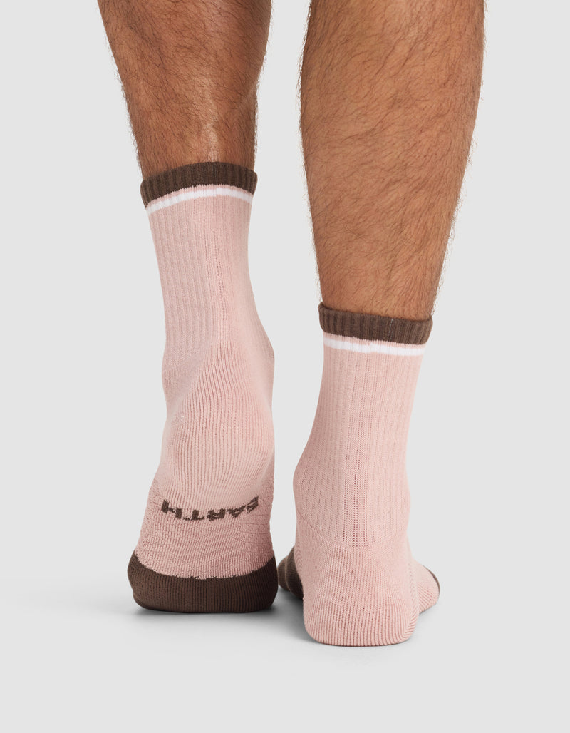 A close-up of the back of a person's legs wearing Cozy Earth Essential Calf Socks in light pink with brown cuffs, heels, and toes. "EARTH" is written on the soles.