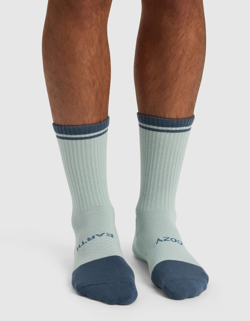 A person wearing Cozy Earth’s Essential Calf Sock – Last Chance in light blue with dark blue toes, heels, and cuffs. "EARTH" is written on the left sock top and "COZY" on the right.