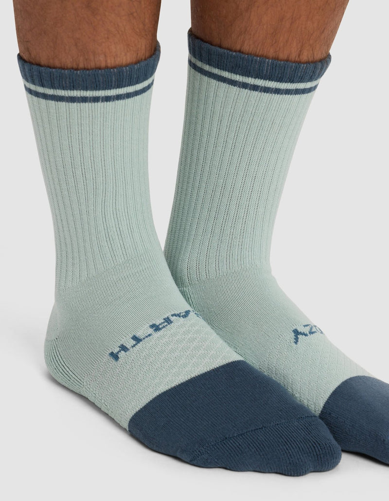 A close-up of lower legs wearing Cozy Earth's Essential Calf Sock - Last Chance: light blue crew socks with dark blue toes, heels, and cuffs, thin dark blue stripes near the top, and text printed on the tops of the feet.