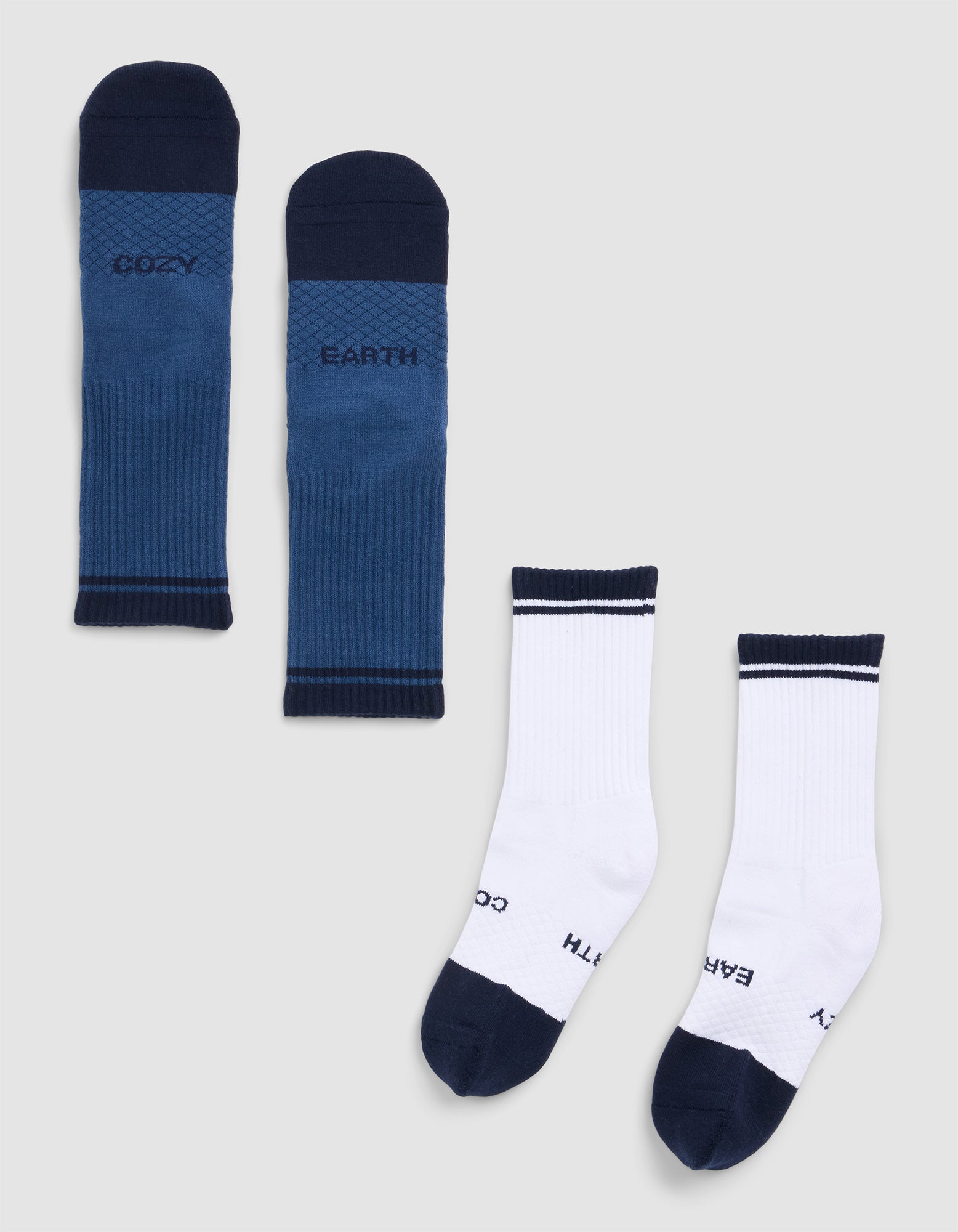 Two pairs of Cozy Earth Essential Calf Socks laid flat: one dark blue pair with "COZY" and "EARTH" text, the other white with dark blue toes, heels, cuffs, and matching text on the toes. 