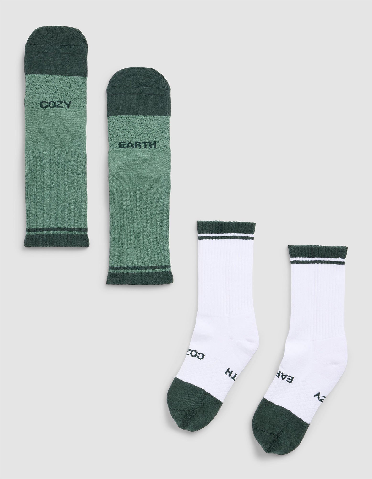 Two pairs of Cozy Earth Essential Calf Socks on a light gray background: one green pair with "COZY EARTH" lettering, and one white pair with green trim and the same words near the toes. 
