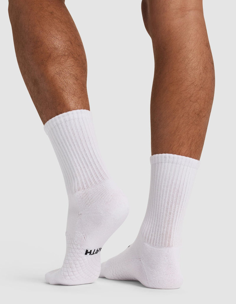 A person with medium skin tone stands on tiptoe, wearing Cozy Earth Essential Calf Socks in white. The ribbed crew socks feature a subtle texture and a small black logo near the sole, set against a plain white background.