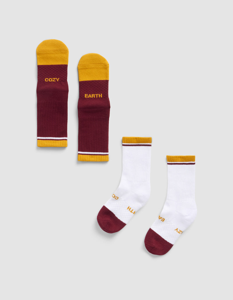 Four Cozy Earth Essential Calf Socks are shown: two burgundy and yellow with "COZY" and "EARTH" text, and two mostly white with burgundy toes, yellow/burgundy cuffs, and small "COZY EARTH" text, all on a light background.