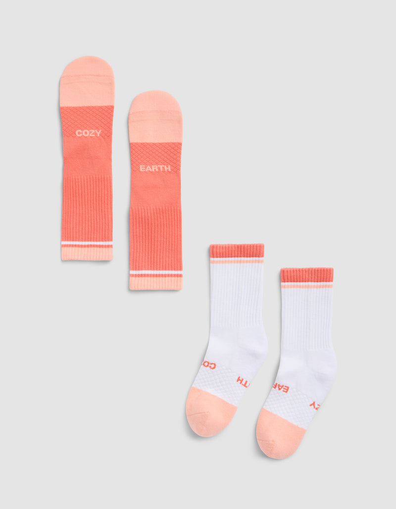 The Essential Calf Sock by Cozy Earth includes two pairs: one mainly coral pink, the other mostly white with coral pink toes, heels, and cuffs. Both have "COZY" and "EARTH" printed on the soles.
