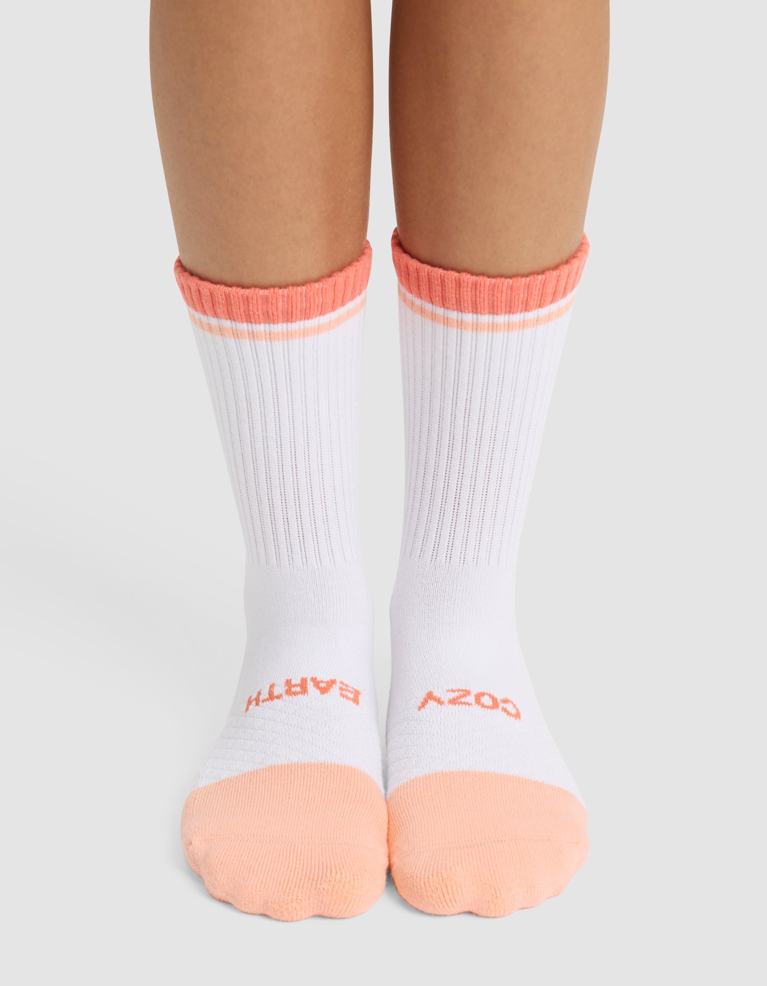 A person wearing Cozy Earth Essential Calf Socks in white with peach toes, heels, and cuffs. "COZY" is printed on the right sock and "BATH" on the left sock in peach lettering near the toes. |Color:Cantaloupe