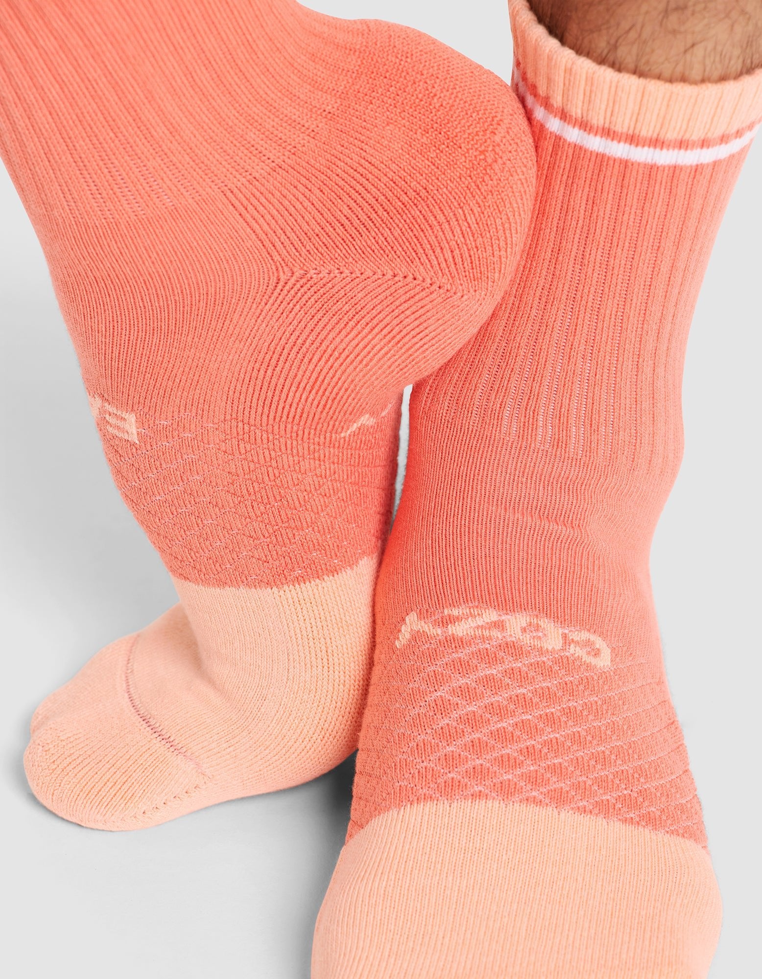 Close-up of a person wearing Cozy Earth Essential Calf Socks in peach and light pink with a textured pattern, white logo, and a white stripe near the top, standing on a light gray surface. 