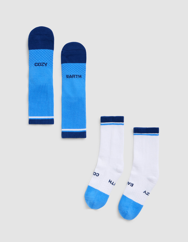 Four Essential Calf Socks by Cozy Earth are laid flat on a light gray background: two bright blue with dark blue toes and cuffs, and two white with blue accents. Each sock features the Cozy Earth branding.
