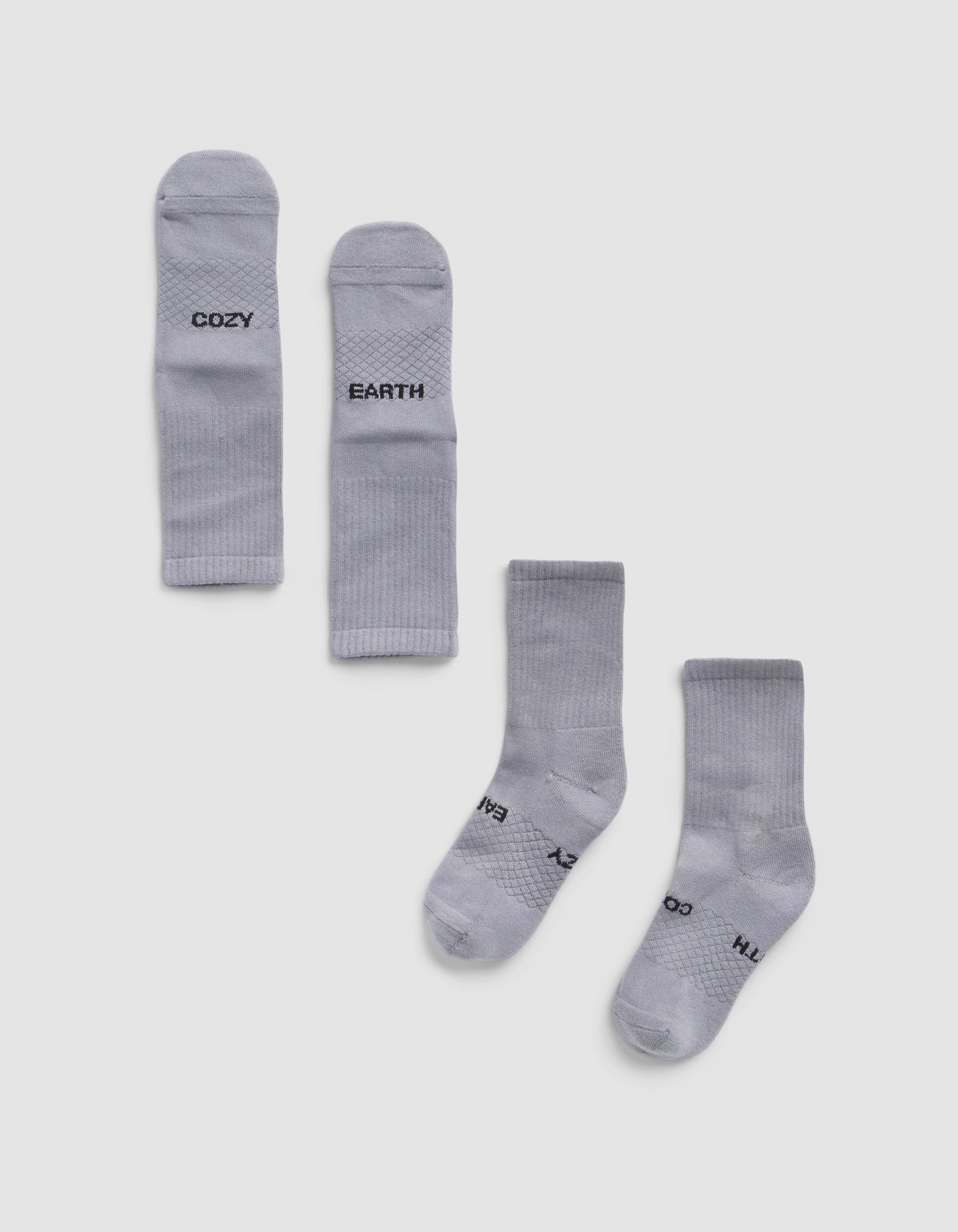 Two pairs of Essential Calf Socks by Cozy Earth are displayed on a white background—one pair folded to show "COZY" and "EARTH," the other flat with the same words visible on the soles.