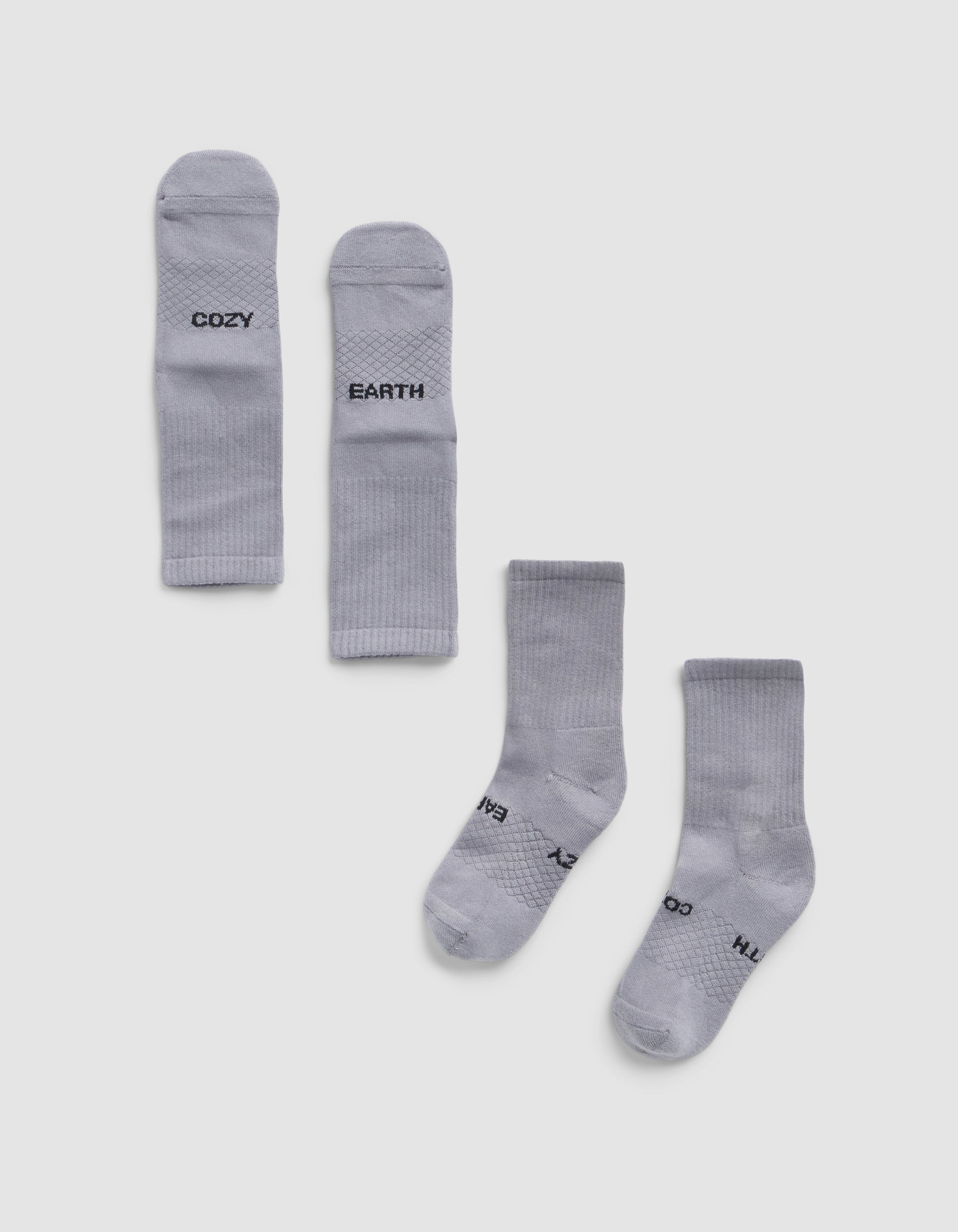 Two pairs of Essential Calf Socks by Cozy Earth are displayed on a white background—one pair folded to show "COZY" and "EARTH," the other flat with the same words visible on the soles.|Color:Stone