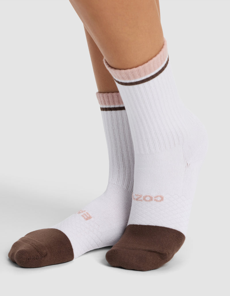 A person wearing Cozy Earth Essential Calf Socks—white with brown toes and heels, light pink cuffs, and a thin brown stripe near the top—stands on a light surface.