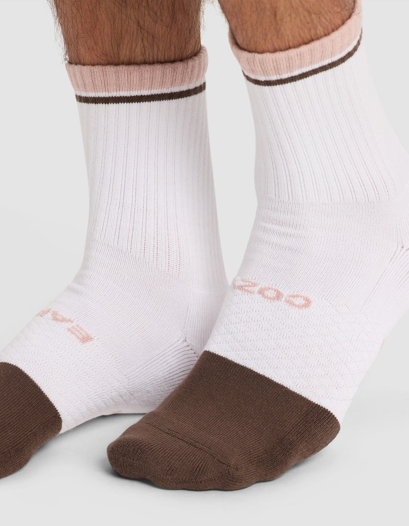 Two feet wear Cozy Earth Essential Calf Socks—white ribbed socks with brown toes and soles, pink accents at the top, a thin brown ankle stripe, and subtle pink text.