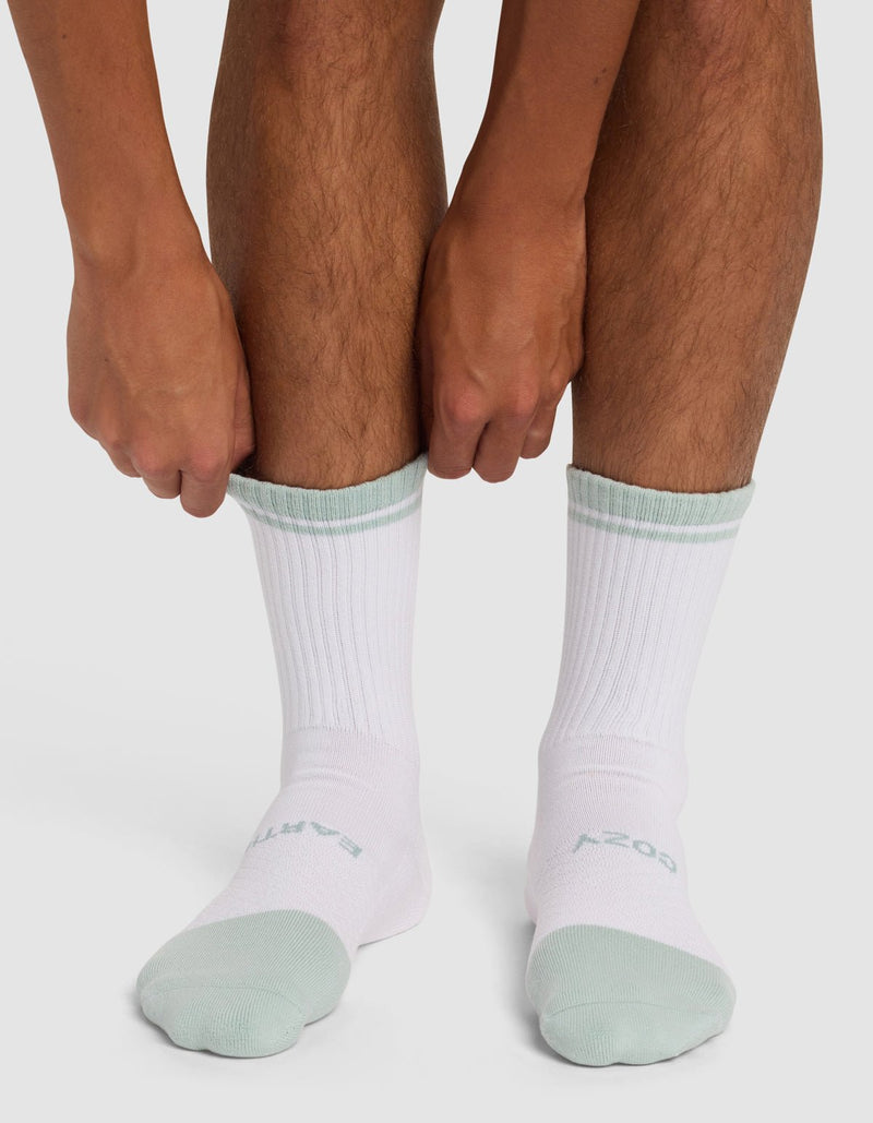 A person pulls on Cozy Earth’s Essential Calf Sock - Last Chance in white with light green trim and faint text atop the foot. The ribbed crew socks are shown on bare legs against a white background.