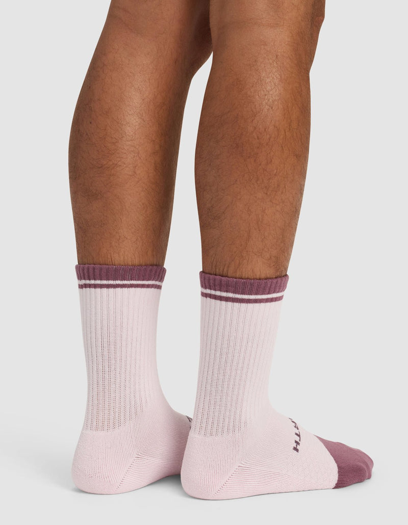 A person stands on a white background, shown from the back at calf height, wearing Cozy Earth’s Essential Calf Sock - Last Chance in light pink with maroon toes, heels, and stripes at the top.