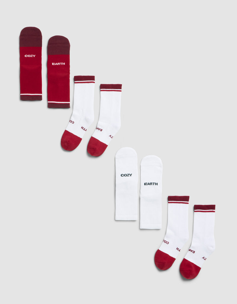 The Cozy Earth Essential Calf Sock 4-Pack includes four pairs: one solid burgundy, two white with red accents, and one white pair featuring "COZY" and "EARTH" text on each sock, displayed diagonally on a light gray background.