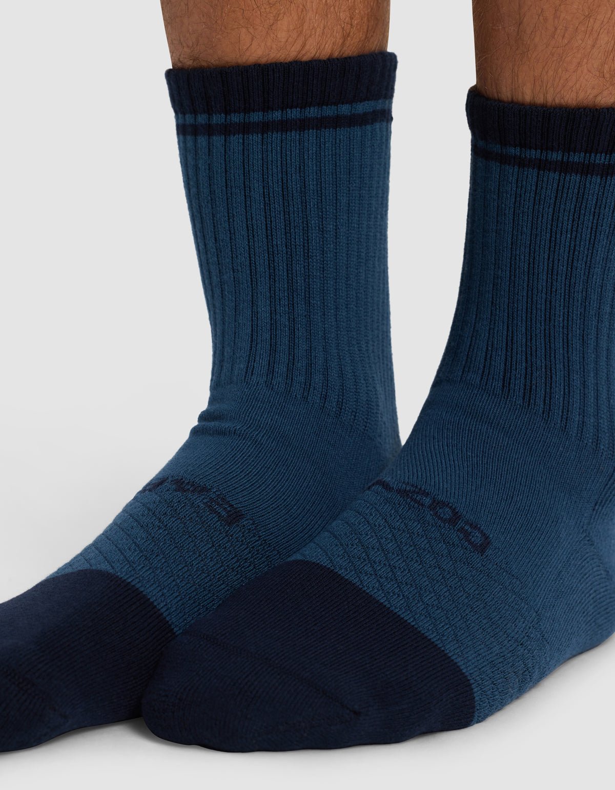 Close-up of a person wearing Cozy Earth Essential Calf Sock - Last Chance, featuring ribbed blue fabric, darker blue toe, heel, and cuff, plus a subtle stripe near the top and text on the foot.