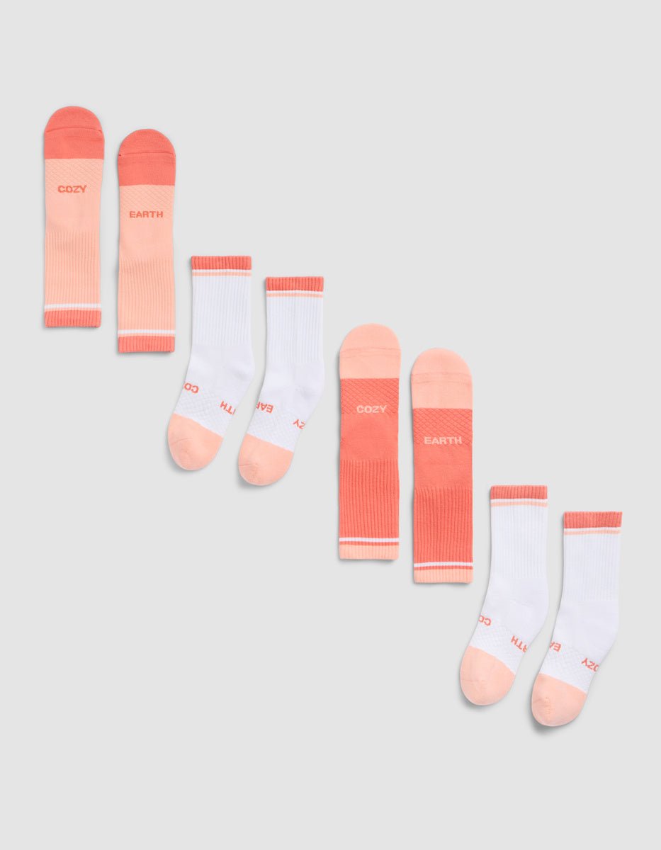 The Cozy Earth Essential Calf Sock 4-Pack, in pink and white shades with "COZY" and "EARTH" near the toes, is arranged diagonally on a light gray background. 