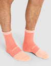 A person wears Cozy Earth Essential Calf Socks in peach with white text and accents, featuring ribbed cuffs and textured panels, standing on a light gray background. Only their lower legs and feet are visible.  |Color:Cantaloupe