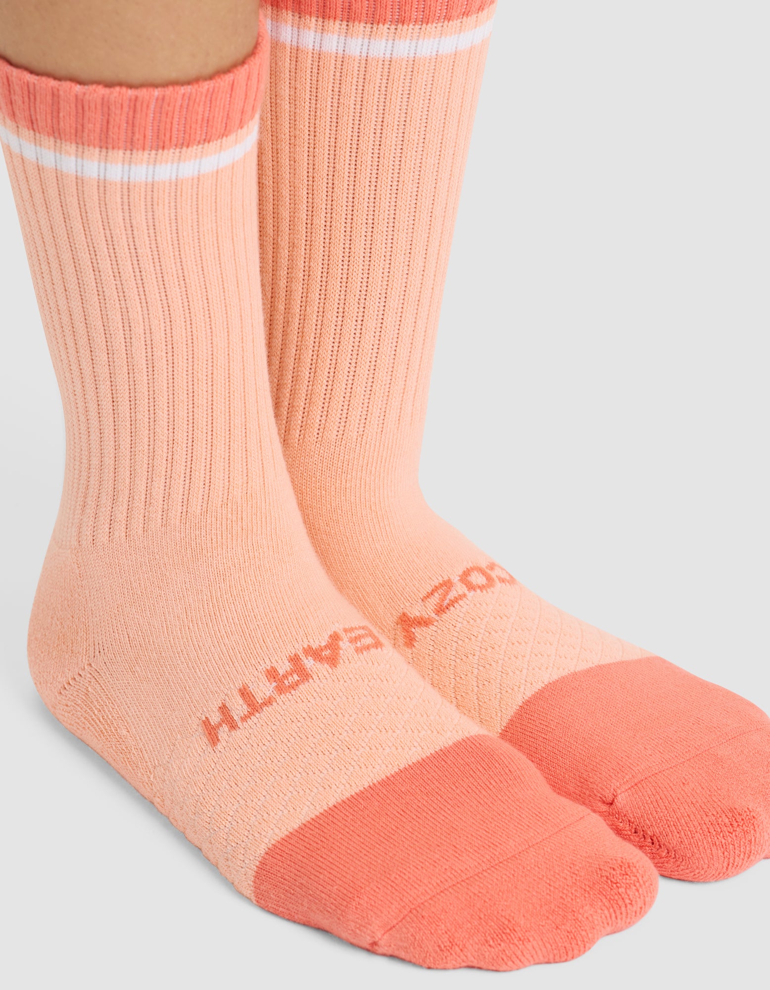 Two feet in Cozy Earth Essential Calf Socks—peach-colored with a darker peach toe and heel, a white stripe near the top, and "COZY EARTH" printed across the top of the foot. 