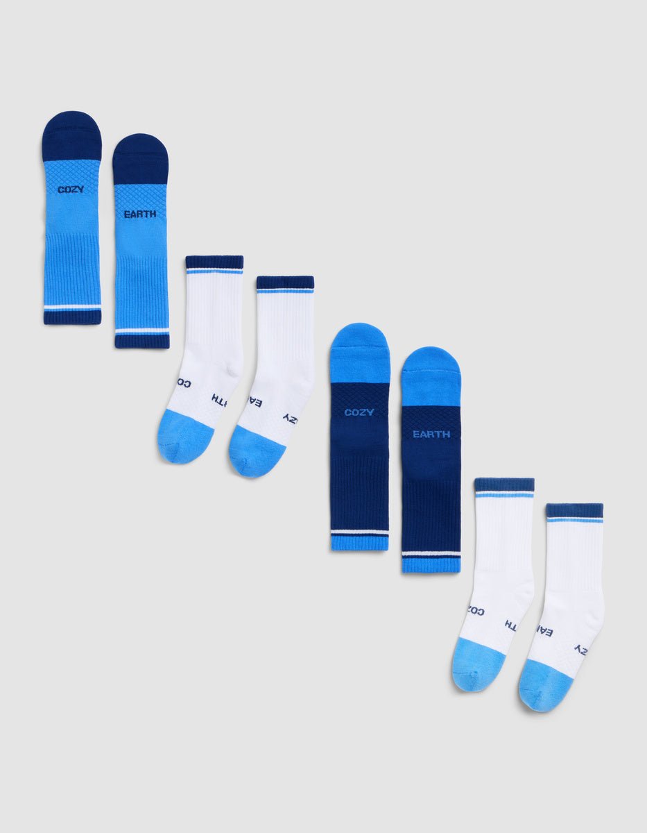 The Essential Calf Sock 4-Pack by Cozy Earth is displayed diagonally on a light gray background, featuring blue and white color-blocked designs with visible text on the sides and soles. 