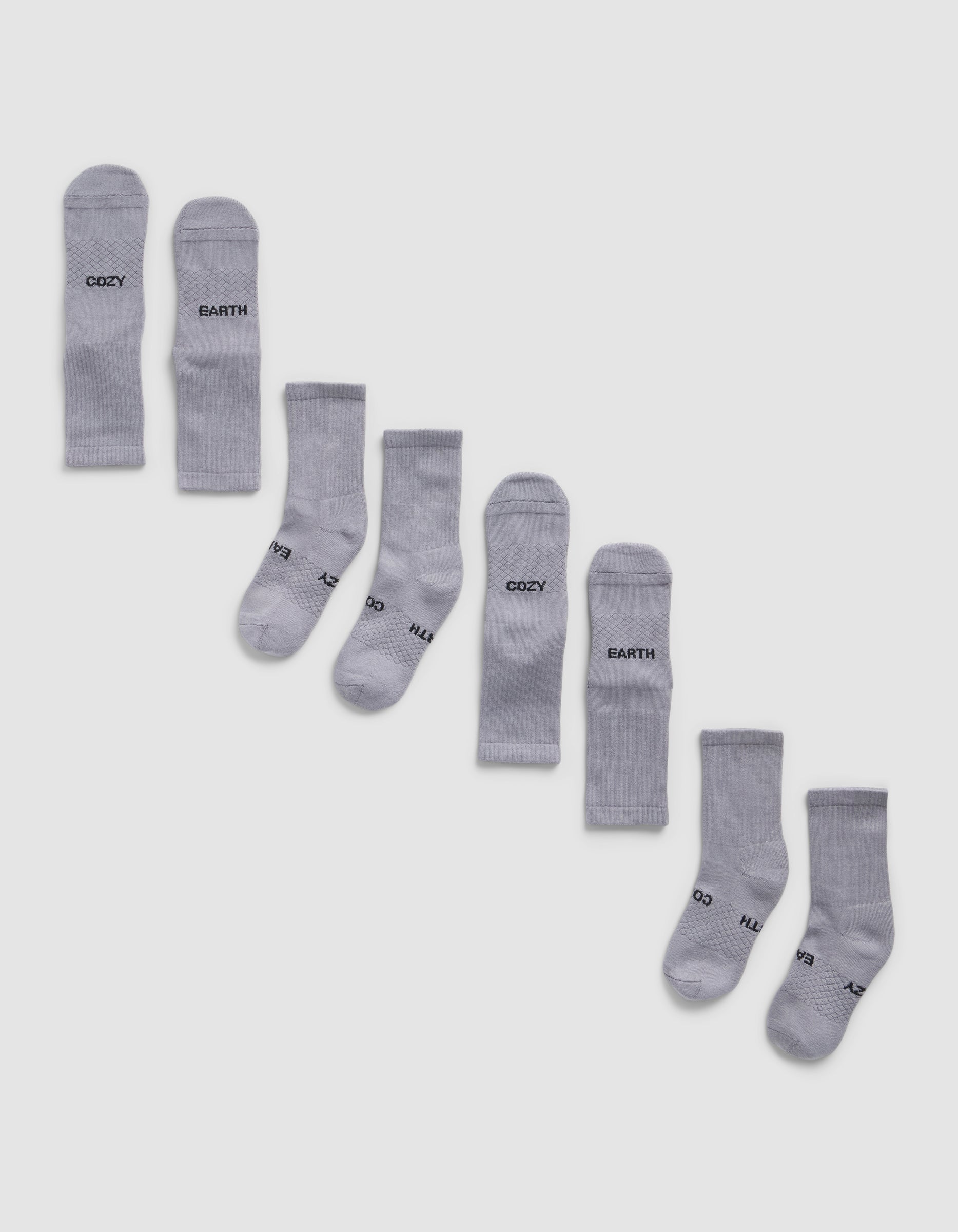 Eight pairs of Cozy Earth Essential Calf Socks, shown side by side in light gray on a white background, display both top and bottom views. Some socks feature black text near the cuffs and toes.|Color:Stone