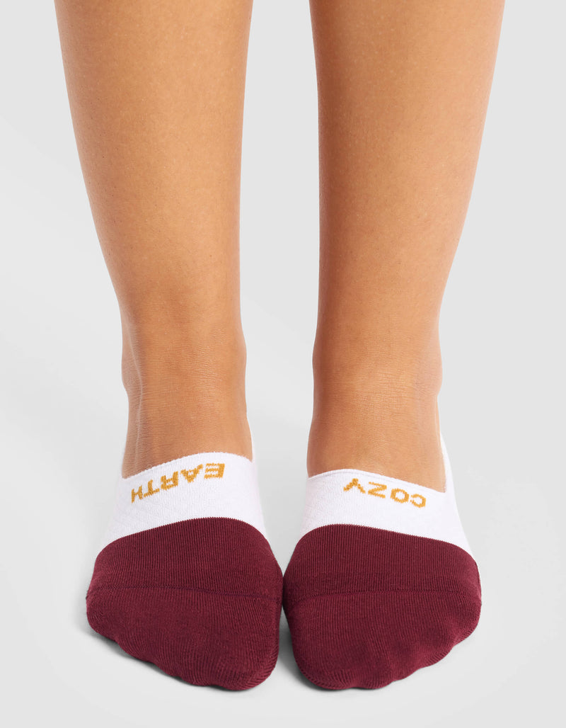 A woman wears Cozy Earth Women's Essential No-Show Socks in white and maroon, featuring "EARTH" on the left and "COZY" on the right sock, both written in yellow across the top.