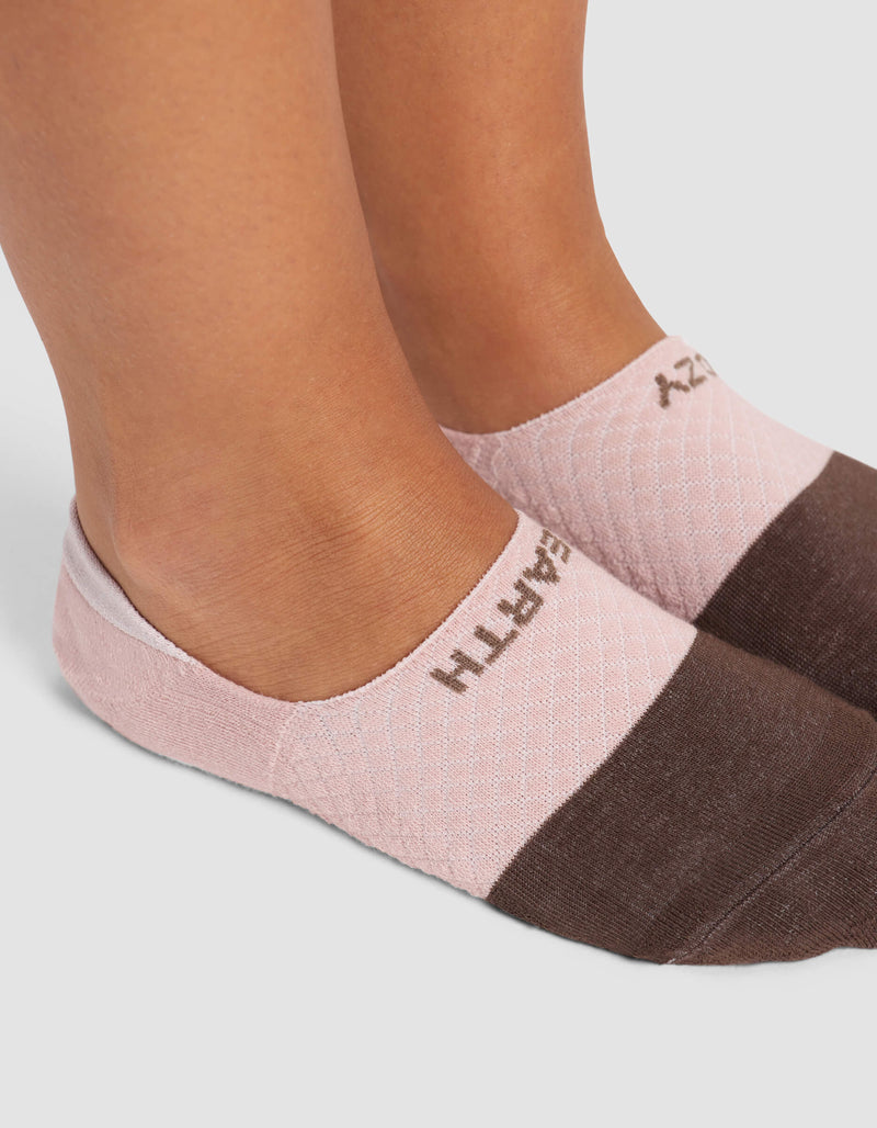 Close-up of a person's feet wearing Cozy Earth Women's Essential No-Show Socks in pink and brown, featuring visible text on top. The background is plain white.