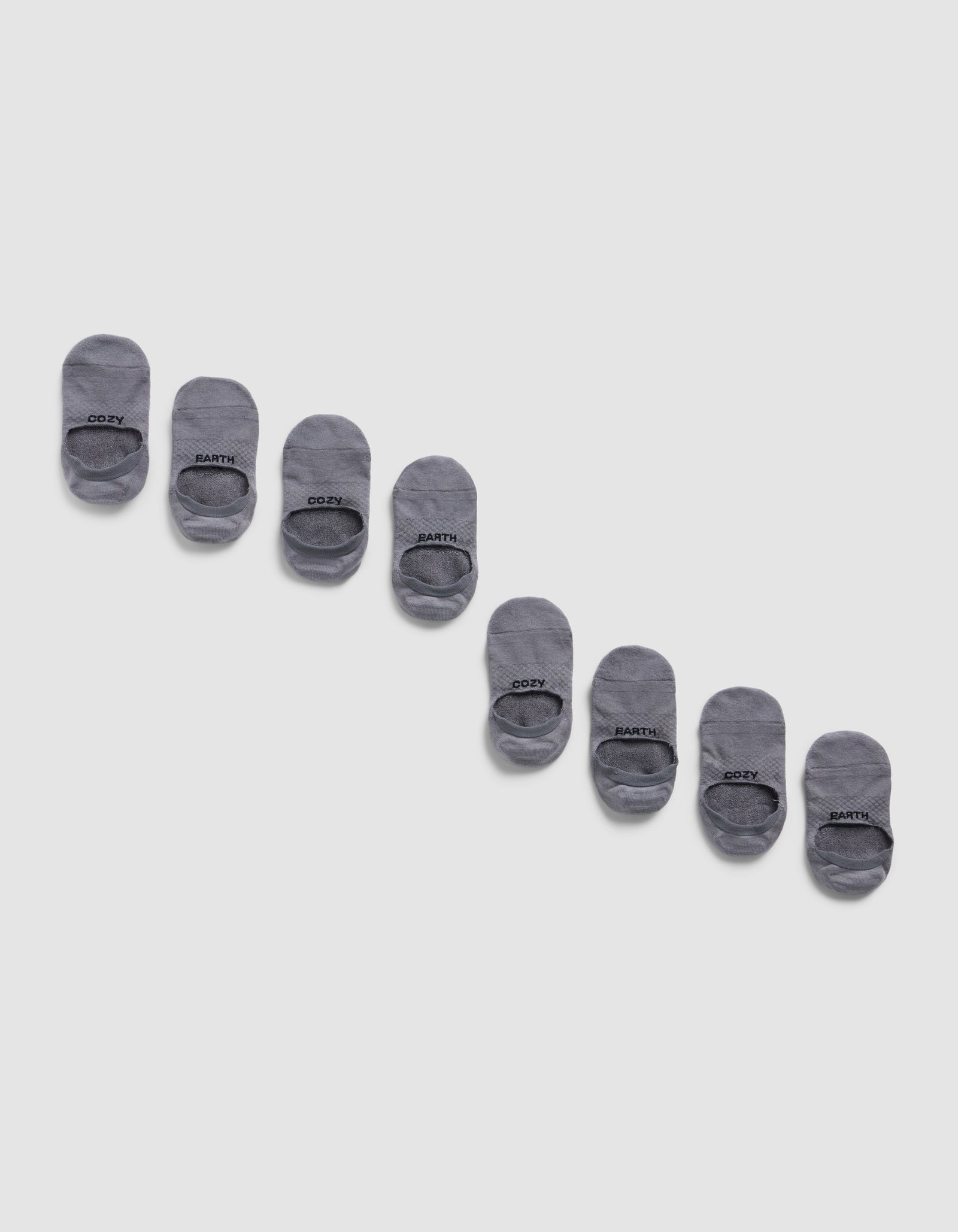 Eight pairs of Cozy Earth Essential No-Show Socks are displayed diagonally on a light gray background, neatly aligned in alternating pairs with black text near the toe.