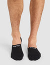 A person with bare legs wears Cozy Earth Essential No-Show Socks in black, featuring "EARTH" on the left and "COZY" on the right in white text. The background is plain and light-colored. |Color:Black