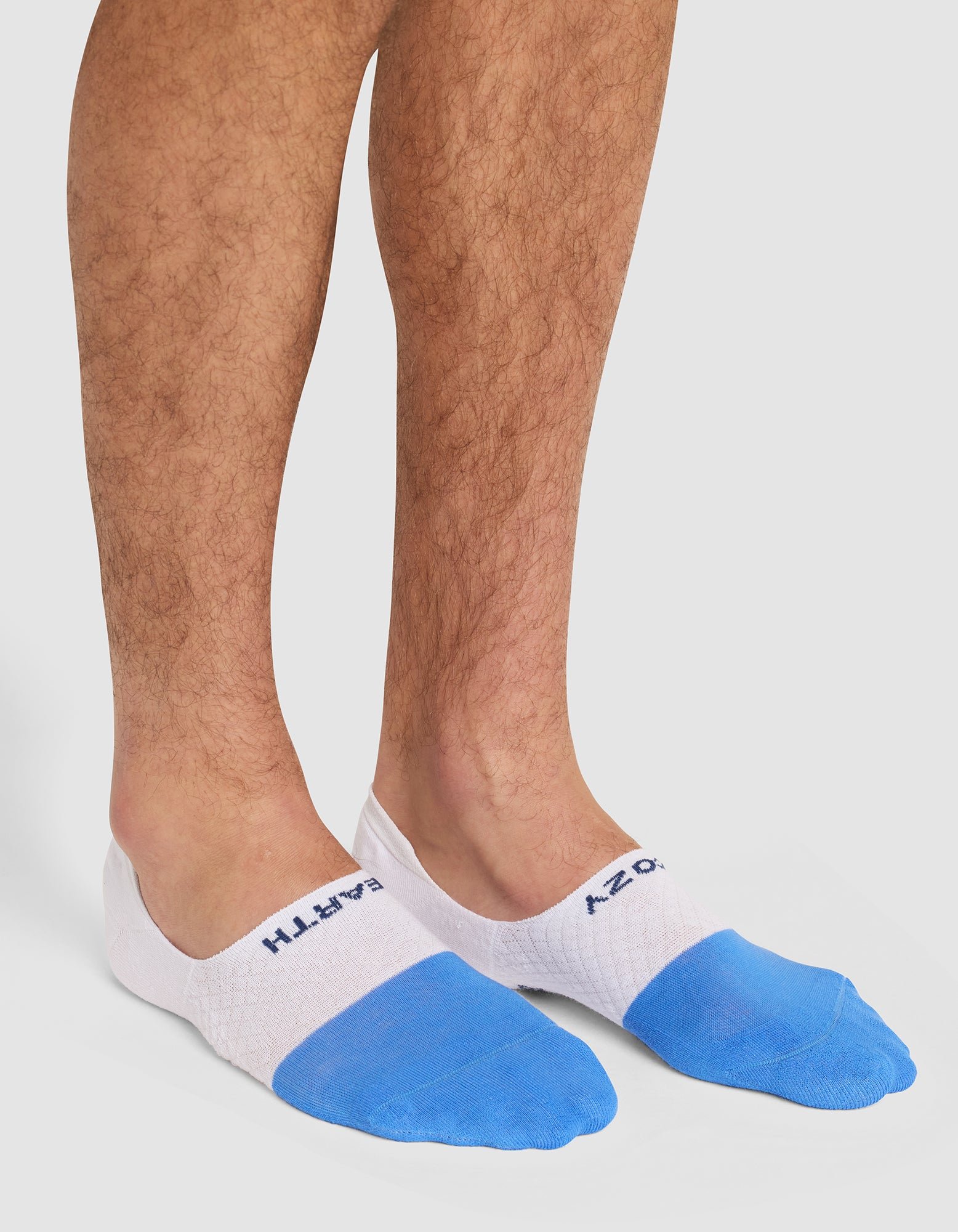 A person wearing Cozy Earth's Essential No-Show Sock in white and blue with visible text near the ankle, standing on a white background. |Color:Harbor