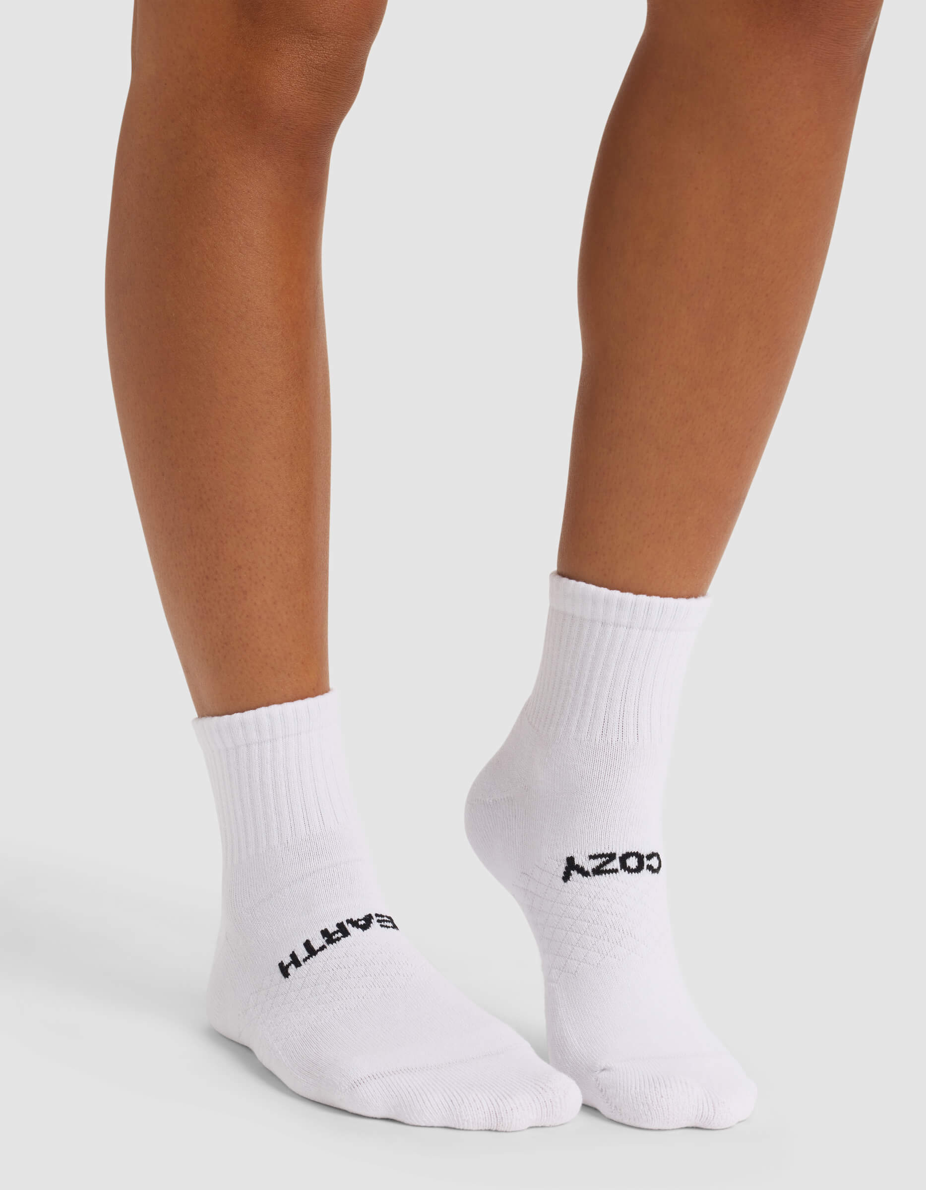 A person wears white Cozy Earth Women's Essential Quarter Socks with "EARTH" on the left and "COZY" on the right, against a plain, light background.