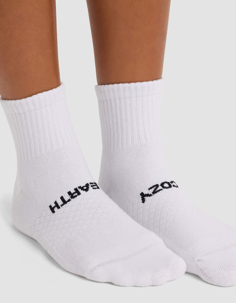 A person wears Cozy Earth's Women's Essential Quarter Socks—white with black text, "EARTH" on the left and "COZY" on the right. The socks feature ribbed tops and are shown against a plain white background.