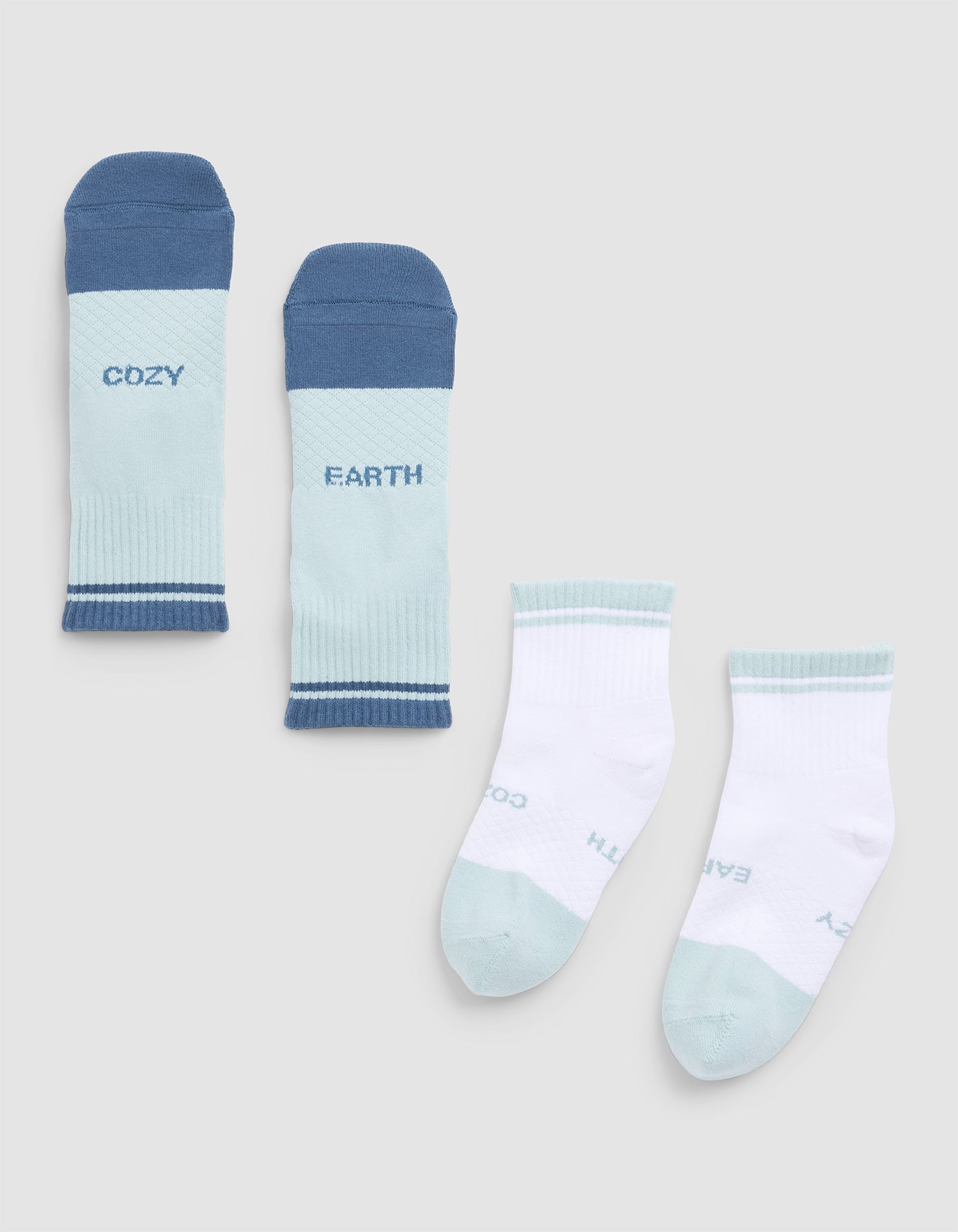 The Essential Quarter Sock by Cozy Earth includes four pairs—two in pastel blue with "COZY" and "EARTH" text, and two in white with blue accents and partially visible branding. 