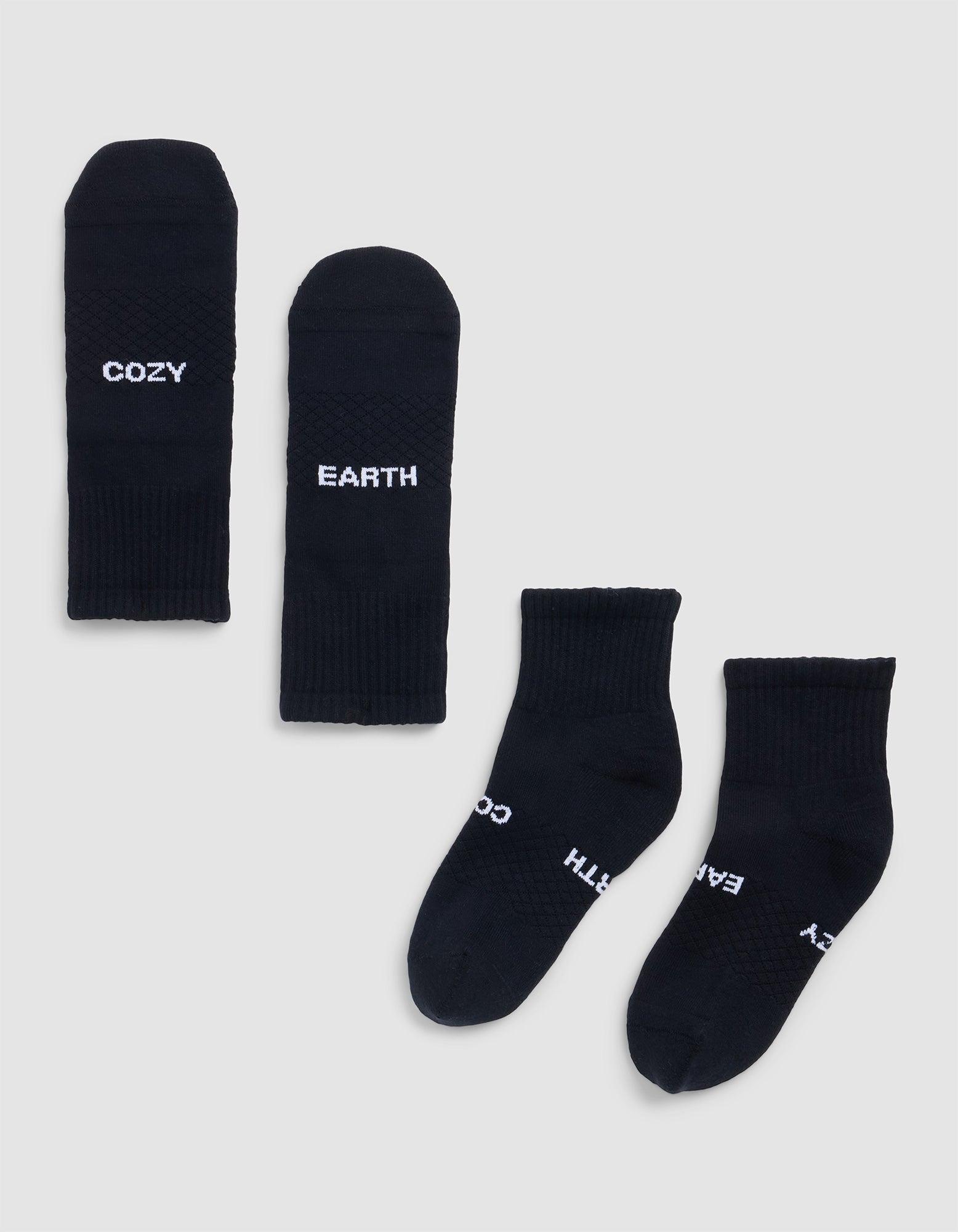 Four Essential Quarter Socks by Cozy Earth are laid out flat on a light background. Two display "COZY" and "EARTH" in white text, while the other pair shows these words partly visible near the toes. 