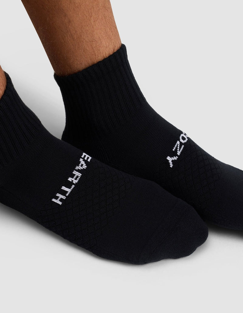 A close-up of two feet wearing Cozy Earth's Essential Quarter Socks in black. "EARTH" is written in white on the left sock and "ZOOM" on the right, set against a light gray background.