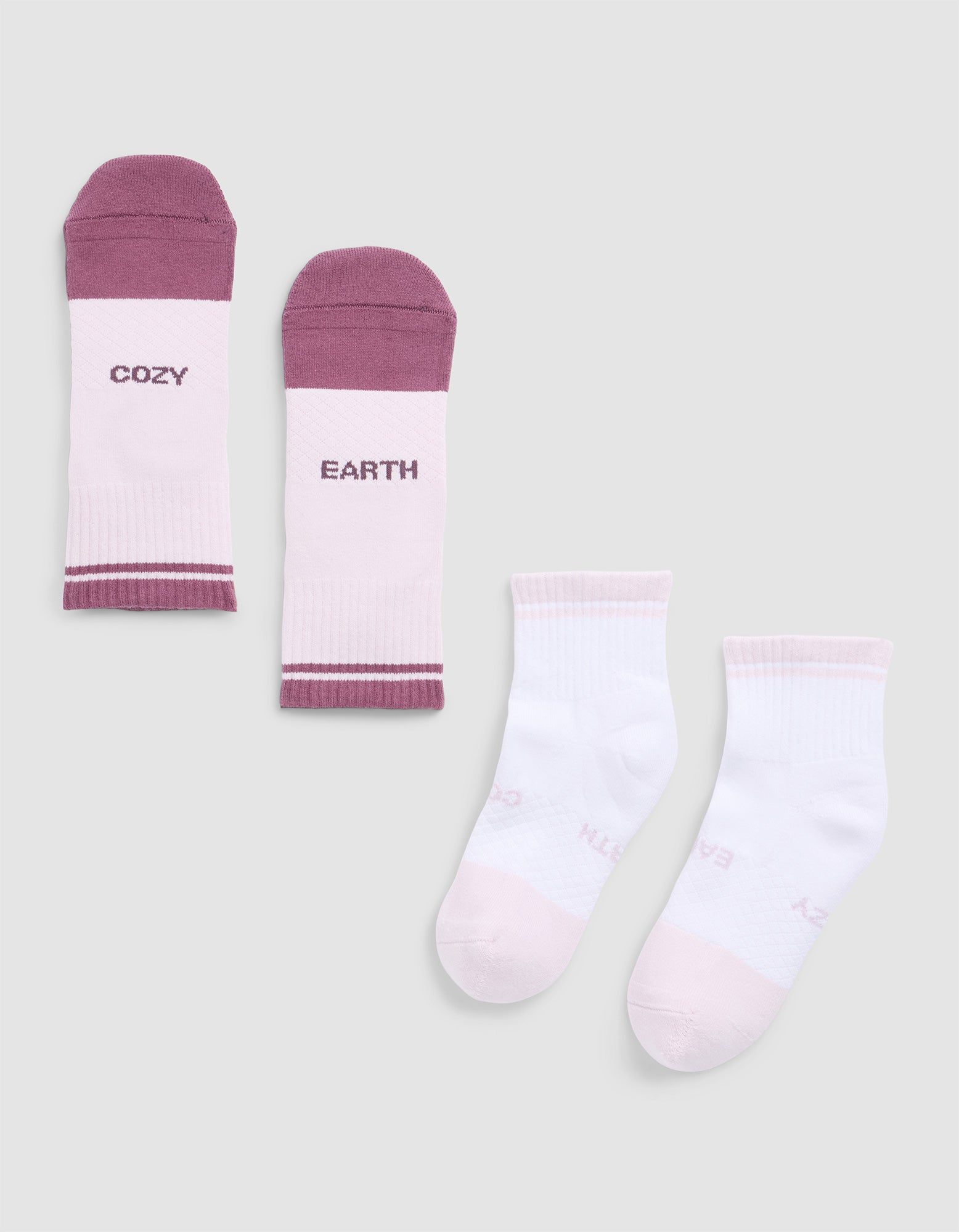 The Cozy Earth Essential Quarter Sock set includes four ankle socks: one pair with white tops and mauve toes and heels reading "COZY" and "EARTH," and one solid white pair with pale pink accents and subtle sole text. 