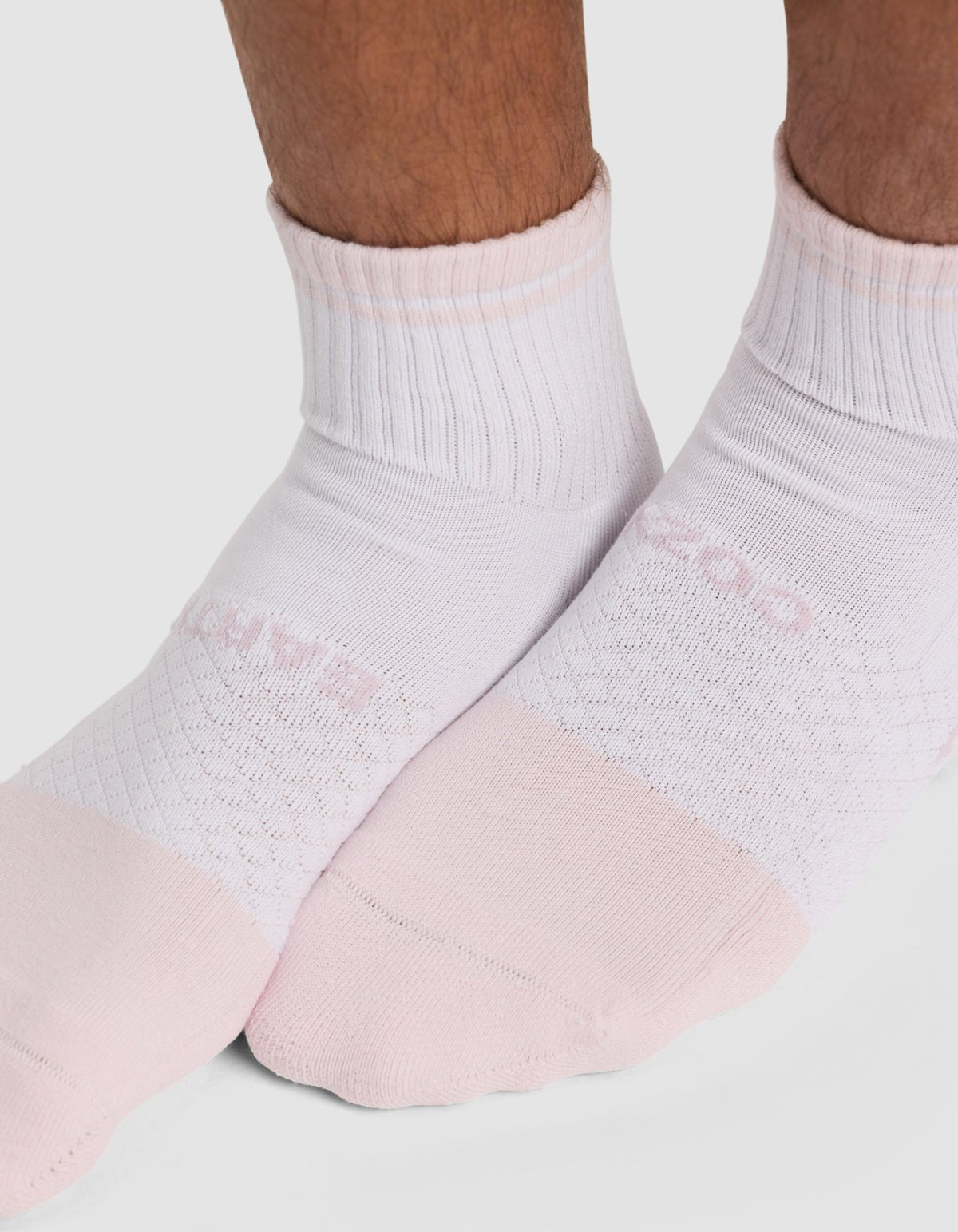 Close-up of a person’s feet wearing Cozy Earth Essential Quarter Sock - Last Chance in light pink and white, standing on a white surface. Only the lower legs and socks are visible. 