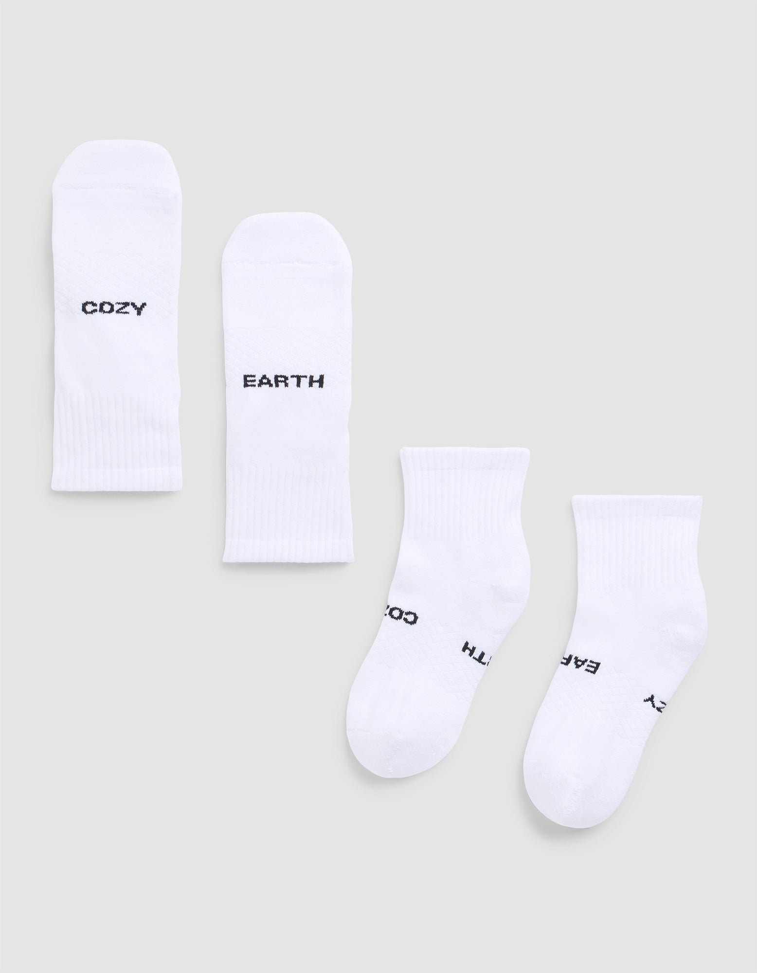 Four white Essential Quarter Socks from Cozy Earth are laid flat on a light gray background. Each features black text: one pair reads “COZY” and “EARTH,” while the other’s text shows parts of “EARTH,” “COZY,” and “OZY.”.  |Color:White