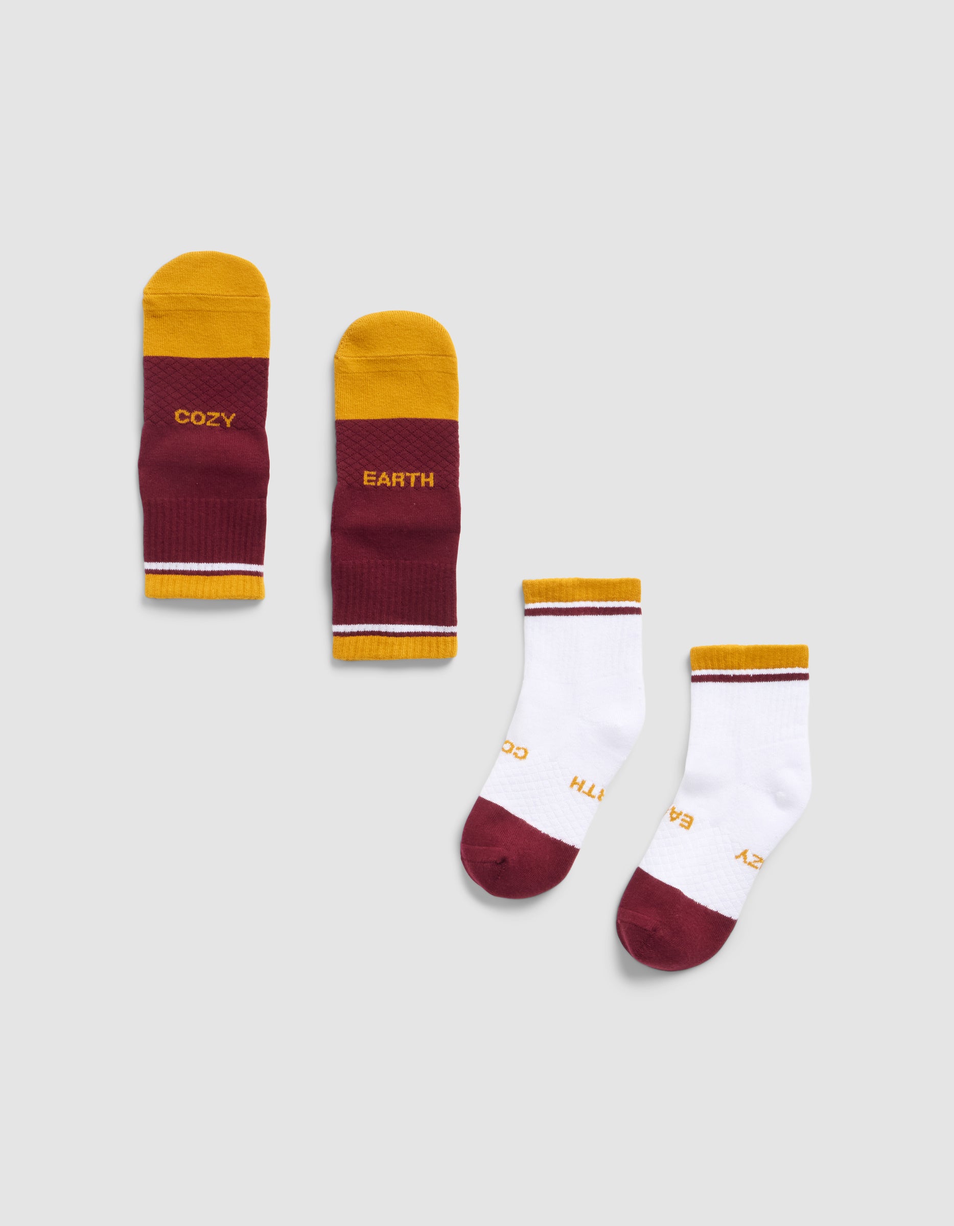 Two pairs of Cozy Earth Essential Quarter Socks: one maroon/yellow pair with "COZY" and "EARTH" on the soles, and one mostly white pair with maroon toes and yellow heels, both featuring the same branding.