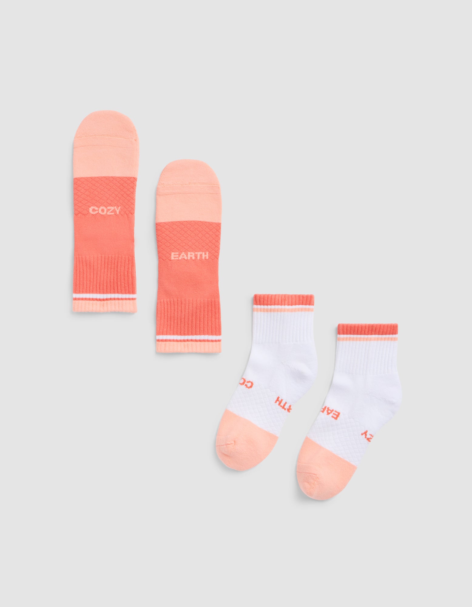 Two pairs of Cozy Earth Essential Quarter Socks: one solid coral with "COZY" and "EARTH" on each sock, and one white pair with coral accents and the same text near the toes, laid flat on a light gray background. 