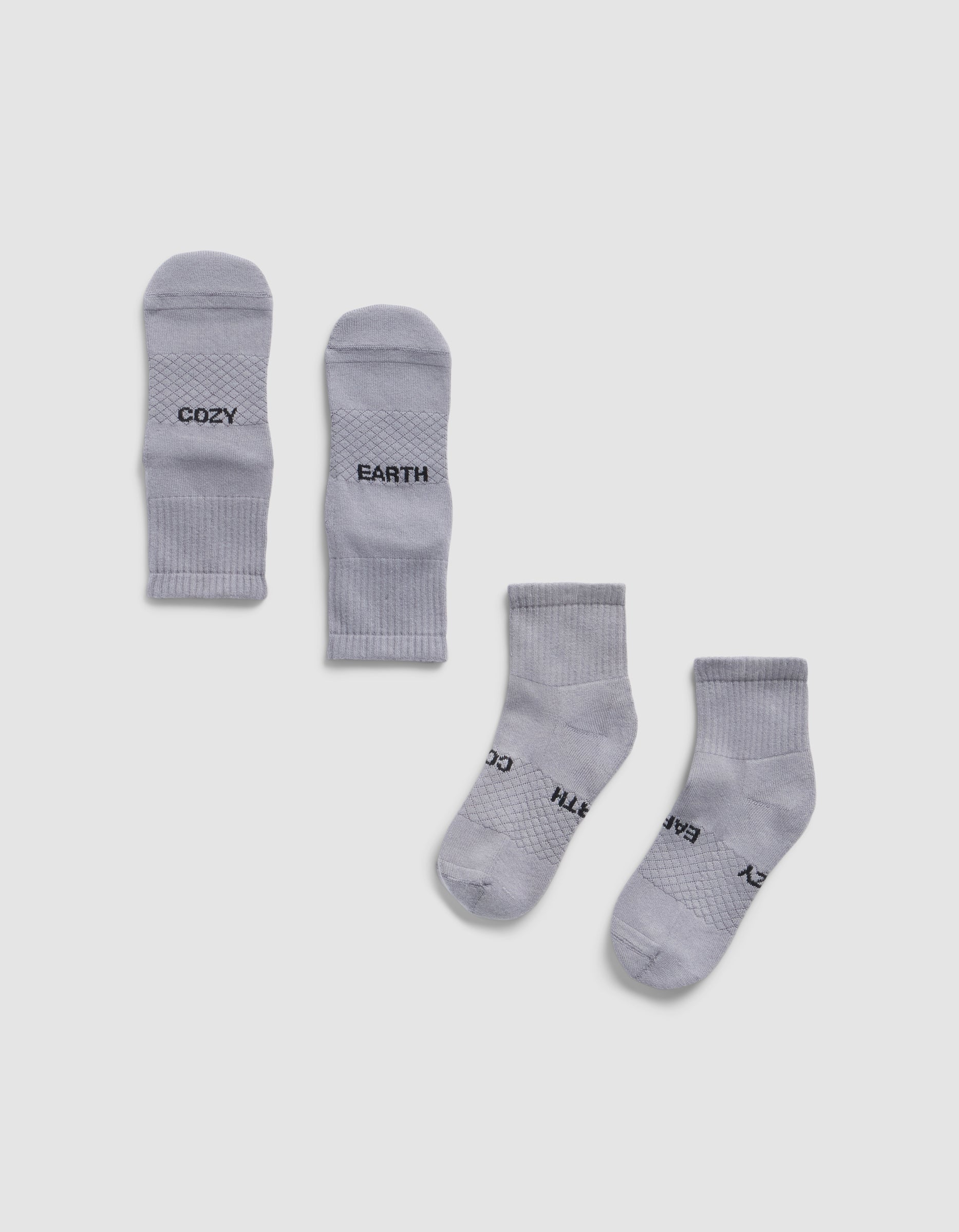 Four Essential Quarter Socks by Cozy Earth in light gray are laid flat on a white background; the top pair displays "COZY" and "EARTH" near the toes, while the bottom pair is oriented with partially visible branding.