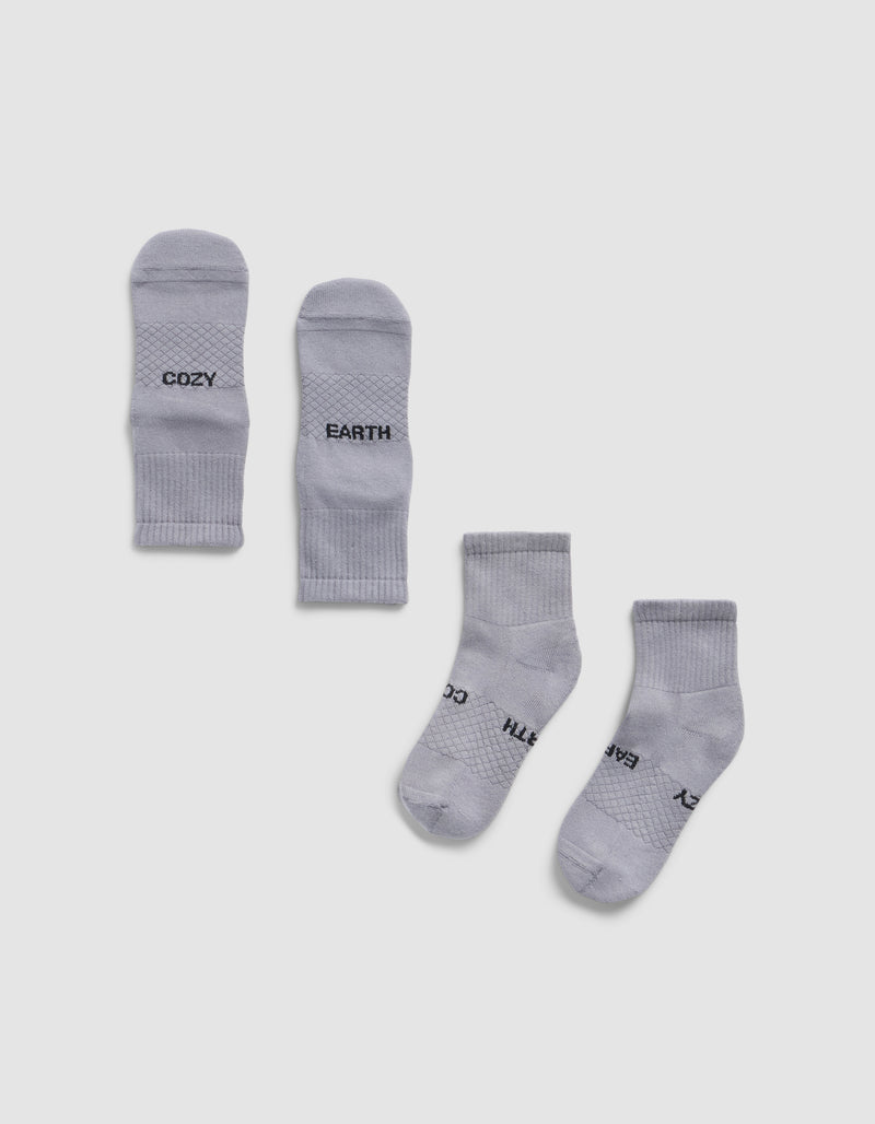 Four Essential Quarter Socks by Cozy Earth in light gray are laid flat on a white background; the top pair displays "COZY" and "EARTH" near the toes, while the bottom pair is oriented with partially visible branding.