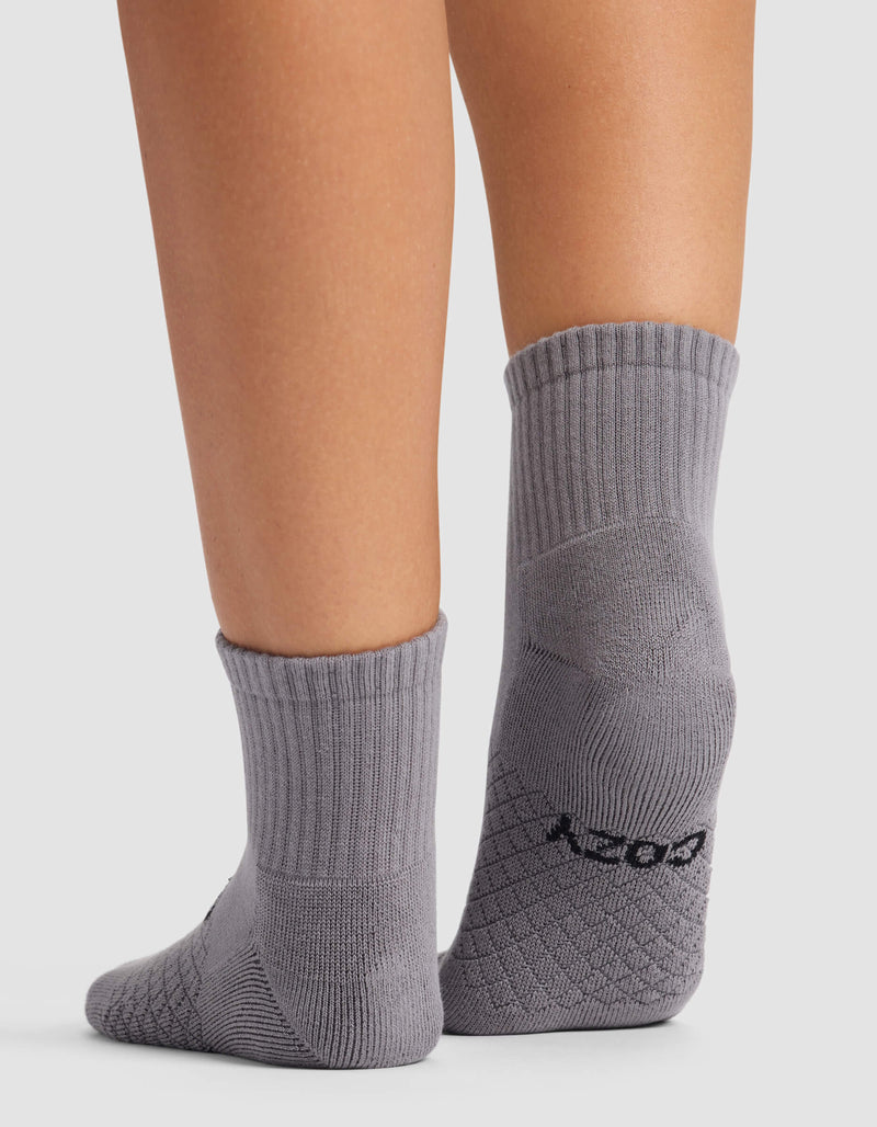 A close-up of the back of a person's lower legs wearing Cozy Earth Women's Essential Quarter Socks in gray with a ribbed texture and black heel lettering, standing on a white background.